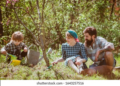 Happy Family: Mother, Father, Children Son On Spring Garden Background. Beautiful Young Smiling Family Having Fun At Farm Yard. Spring Gardening Routine