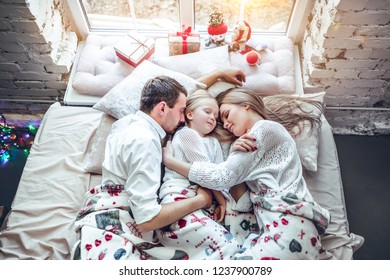 Happy family, mother, father and daughter resting on the white bed. Christmas decorations.
