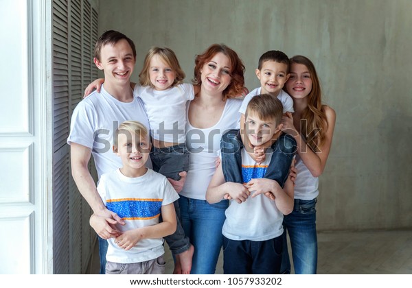 Happy\
family mother, father and five children near the wall at home.\
Woman, man and little kids relax in a white bedroom. Happy family\
at home. Young parents playing whith their\
children