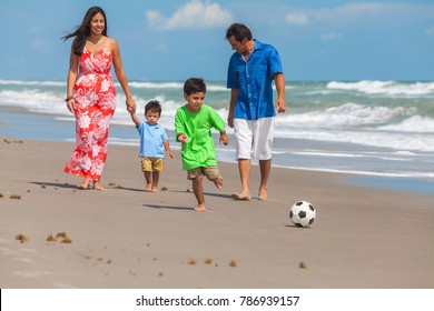 A happy family of mother, father parents & two boy son children, playng football or soccer and having fun in the sand of a sunny beach - Powered by Shutterstock