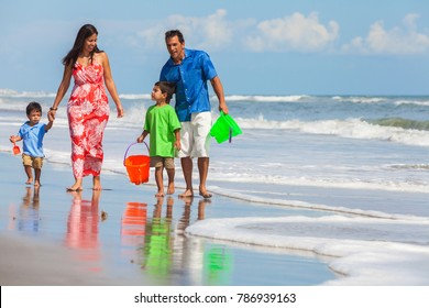 A Happy Family Of Mother, Father Parents & Two Boy Son Children, Playng And Having Fun In The Waves Of A Sunny Beach