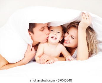 Happy Family, Mother ,father And Their Baby Under The Blanket On The Bed At Home (focus On The Man)