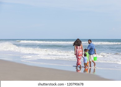 A Happy Family Of Mother, Father And Two Children, Two Boy Sons, Walking And Having Fun In The Sand And Sea Of A Sunny Beach