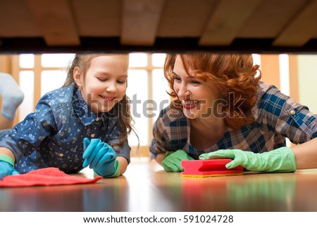 Happy family mother and kid daughter clean room at home. Middle-aged woman and child girl wiped floor under bed