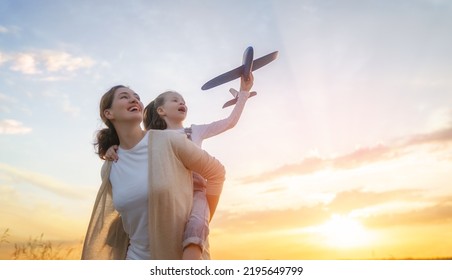 Happy family, mother and kid with toy plane are running through the field at sunset. - Shutterstock ID 2195649799