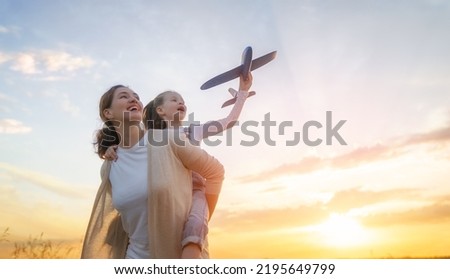 Happy family, mother and kid with toy plane are running through the field at sunset.
