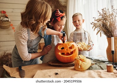 Happy family mother and kids carving pumpkin for Halloween holiday together, preparing for holiday party in kitchen, mom with little daughter and son smiling having fun while creating Jack-o-lantern - Shutterstock ID 2045199506
