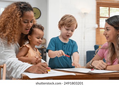 Happy family. Mother and kids together paint. Woman helps the child. Little children with kindergarten teacher drawing at table indoors. Learning and playing - Powered by Shutterstock