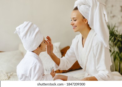 Happy Family Mother And Little Daughter In Dressing Gowns And Towels Laugh And Do Makeup  A Spa Day At Home
