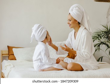 Happy Family Mother And Little Daughter In Dressing Gowns And Towels Laugh And Do Makeup  A Spa Day At Home
