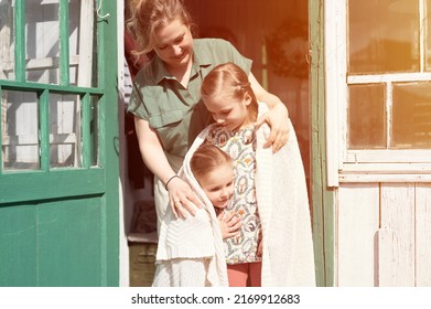 happy family mother with little kids daughters helper have fun in suburb countryside life on laundry day. candid mom hug and cover children with plaid and doing chores on porch of country house. flare