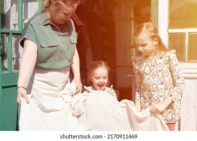 happy family mother with little kids daughters helper girls have fun in suburb countryside life on laundry day. candid mom and children doing chores on porch of country house. people with plaid. flare