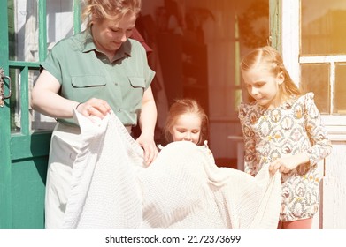 happy family mother with little kids daughters helper girls have fun in suburb countryside life on laundry day. candid mom and children doing chores on porch of country house. people with plaid. flare