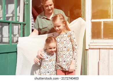 happy family mother with little kids daughters helper have fun in suburb countryside life on laundry day. candid mom hug and cover children with plaid and doing chores on porch of country house. flare