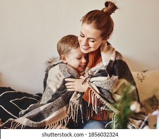 Happy Family Mother And Loving Son Hug And Laugh Wrapped In A Warm Blanket On A Cozy Winter Evening At Home 
