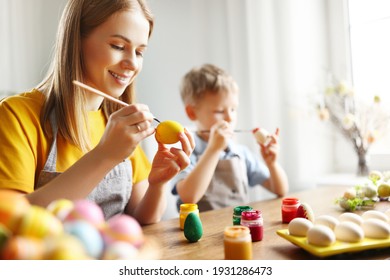 Happy family: mother and son sitting at table at home and painting eggs with gouache while preparing for Easter holiday  