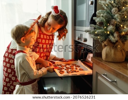 Happy family mother and son taking freshly baked Christmas cookies from oven while cooking together in cozy kitchen during winter holidays, little boy helping mom to prepare for New Year at home