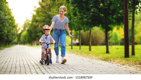 Happy Family Mother Teaches Child Son To Ride A Bike In The Park In Nature
