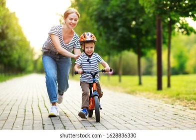 Happy Family Mother Teaches Child Son To Ride A Bike In The Park In Nature
