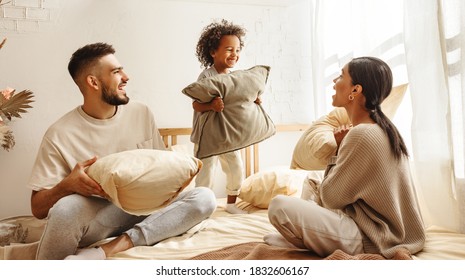 Happy Family Multi Ethnic Mother, Father And Son  Laughing, Playing, Fights Pillows And Jumping In Bed In Bedroom At Home
