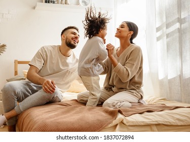 glückliche Familie multiethnische Mutter, Vater und Sohn lachen, spielen und im Schlafzimmer zu Hause springen