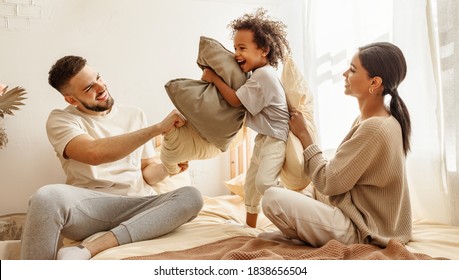 happy family multiethnic mother, father and son  laughing, playing, fights pillows and jumping in bed in bedroom at home