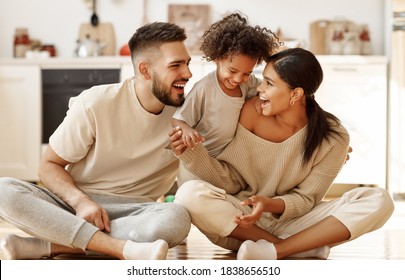 Happy Family Multiethnic Mother, Father And Son  Laughing, Playing,and Tickles  On Floor In Cozy Kitchen At Home
