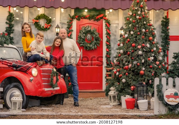  Happy\
family near house decorated for Christmas.Street Christmas decor\
with red car and Christmas veranda decorations.Soft selective\
focus, art noise.Ukraine. Odessa 19 November\
2021