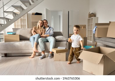 Happy Family New Home Owners With Child Son In Living Room On Moving Day. Young Couple Apartment Buyers Relaxing On Couch With Kid Boy Playing Around Boxes. Relocation And House Renovation, Removal.