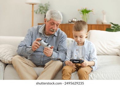 Happy family. Old senior man grandfather boy grandson playing video game with joysticks at home. Smiling grandparent and child using gamepads for video game. Older generation modern tech usage - Powered by Shutterstock