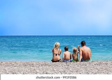 Happy Family On The Beach. Mother Dad Daughter And Son Sitting Back On Beach