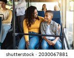 Happy Family On The Bus. Portrait of smiling young African American woman and boy sitting and going on a public transport, lady hugging son and looking at each other, enjoying ride or travel