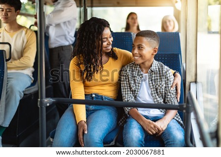 Happy Family On The Bus. Portrait of smiling young African American woman and boy sitting and going on a public transport, lady hugging son and looking at each other, enjoying ride or travel