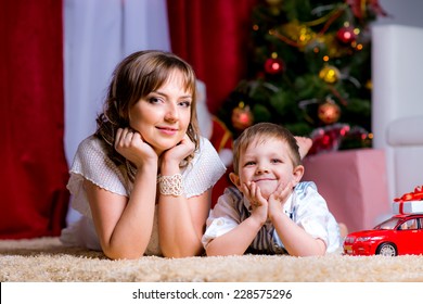 Happy Family On The Floor In The Christmas Evening With Gifts At The Christmas Tree With Christmas Lights. Children's Car,