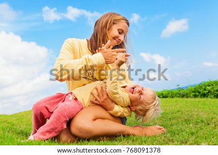 Happy family on green grass lawn. Child have fun on outside walk - mother tickling funny baby son lying on her laps. Active people activity on tropical holiday with kid. Summer lifestyle background.