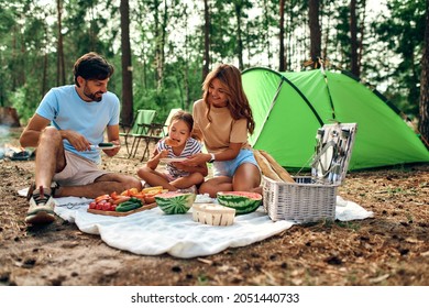 Happy family on a picnic sit on a blanket near the tent in the forest for the weekend. Camping, recreation, hiking. - Powered by Shutterstock