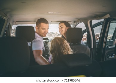 Happy Family On A Road Trip In Their Car. Dad, Mom And Daughter Are Traveling By The Sea Or The Ocean Or The River. Summer Ride By Automobile