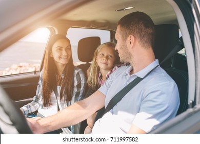 Happy Family On A Road Trip In Their Car. Dad, Mom And Daughter Are Traveling By The Sea Or The Ocean Or The River. Summer Ride By Automobile