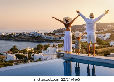 A happy family on summer holidays stands by the swimming pool and enjoys the beautiful sunset behind the mediterranean sea in Greece