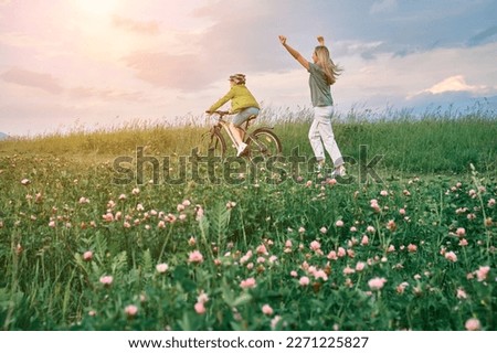 happy family outdoors, Mother teaching son to ride bicycle. Happy cute boy in helmet learn to riding a bike in park on green meadow in summer day at sunset time.