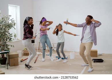 Happy family painting the walls together with white paint in the room dance in the middle of the apartment with brushes in hand sing, parents play with their children