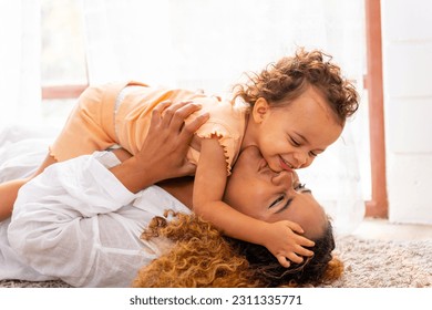 Happy family parent and child spending time together on holiday vacation. Mother playing and hugging little daughter on the floor in living room at home. Parenting and family relationship concept. - Shutterstock ID 2311335771