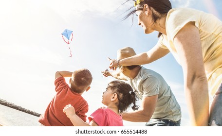 Happy Family With Parents And Children Playing Together With Kite At Beach Vacation - Summer Joy Happiness Concept With Mixed Race People Having Candid Genuine Fun  - Warm Vintage Backlight Filter