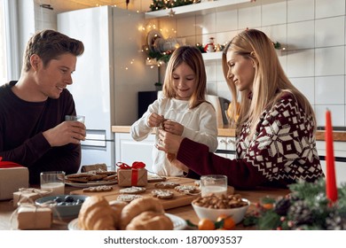 Happy family parents and cute small child daughter making Christmas cookies decorations at home. Young couple mom and dad helping kid preparing gifts having breakfast together on xmas at kitchen table - Powered by Shutterstock