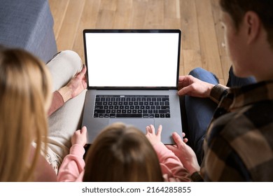 Happy Family Parents And Kid Child Daughter Using Laptop Computer Mock Up White Screen Sitting On Couch At Home Doing Ecommerce Shopping Online Together. Over Shoulder Top View