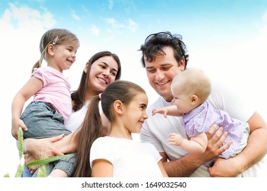 Happy family of parents and three girls hugging and smiling at camera in summer field - Shutterstock ID 1649032540
