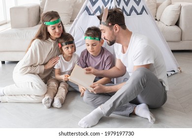 Happy Family Of Parents And Two Children Playing Indian At Home, Wigwam Tent, Feather Roach, Reading Book About Native American Indian Culture