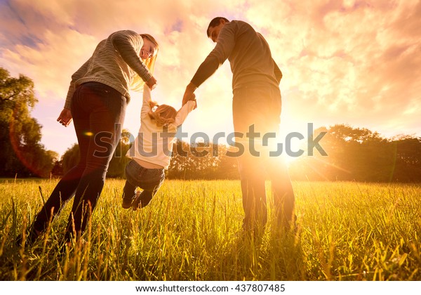 Happy family in the park evening\
light. The lights of a sun. Mom, dad and baby happy walk at sunset.\
The concept of a happy family.Parents hold the baby\'s\
hands.