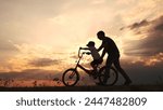 happy family in the park. father teaching son to ride a bike at sunset silhouette in the park. son child learning to ride a bike at sunset father helping son. child playing lifestyle riding bike