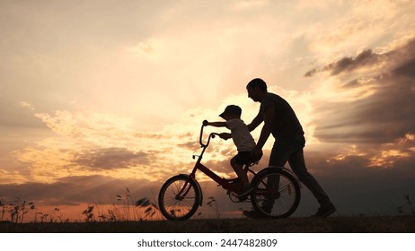 happy family in the park. father teaching son to ride a bike at sunset silhouette in the park. son child learning to ride a bike at sunset father helping son. child playing lifestyle riding bike - Powered by Shutterstock